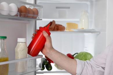 Photo of Man taking ketchup out of refrigerator, closeup