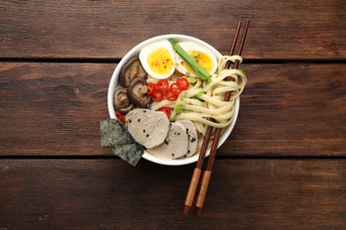 Delicious ramen with meat in bowl and chopsticks on wooden table, top view. Noodle soup