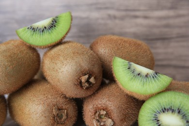 Photo of Heap of whole and cut fresh kiwis near wooden wall, closeup