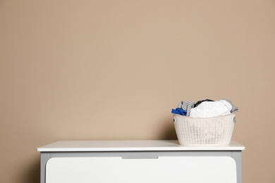 Photo of Plastic laundry basket with dirty clothes on chest of drawers near color wall. Space for text