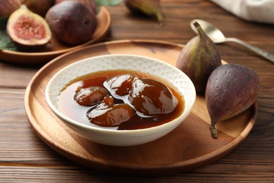 Photo of Bowl of tasty sweet jam and fresh figs on wooden table