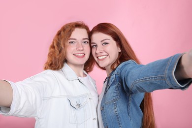 Photo of Beautiful young redhead sisters taking selfie on pink background