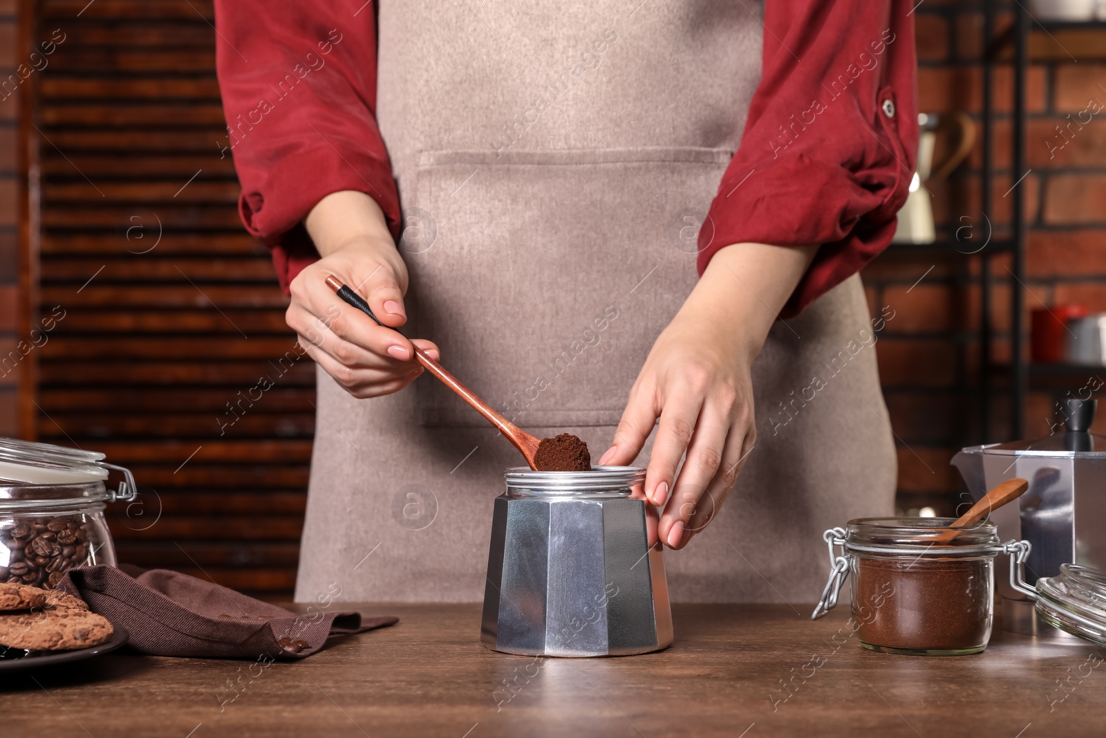 Photo of Woman putting ground coffee into moka pot at wooden table, closeup