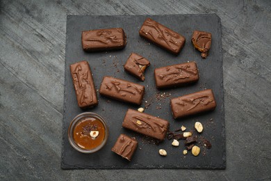 Many tasty chocolate bars with caramel and nuts on grey table, top view
