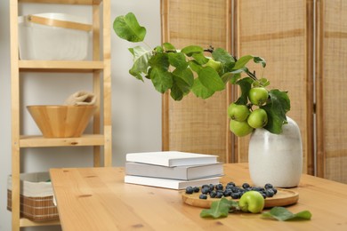 Books, blueberries and branch with green apples on wooden table in room