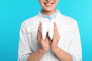 Photo of Female dentist holding tooth model on color background, closeup