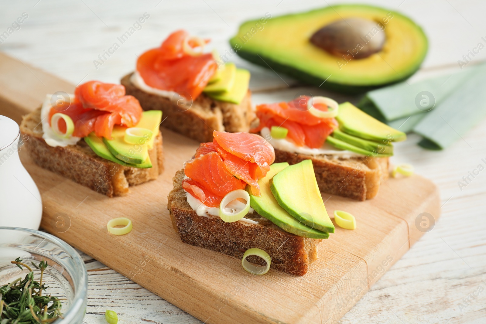 Photo of Tasty sandwiches with fresh sliced salmon fillet and avocado on wooden board, closeup