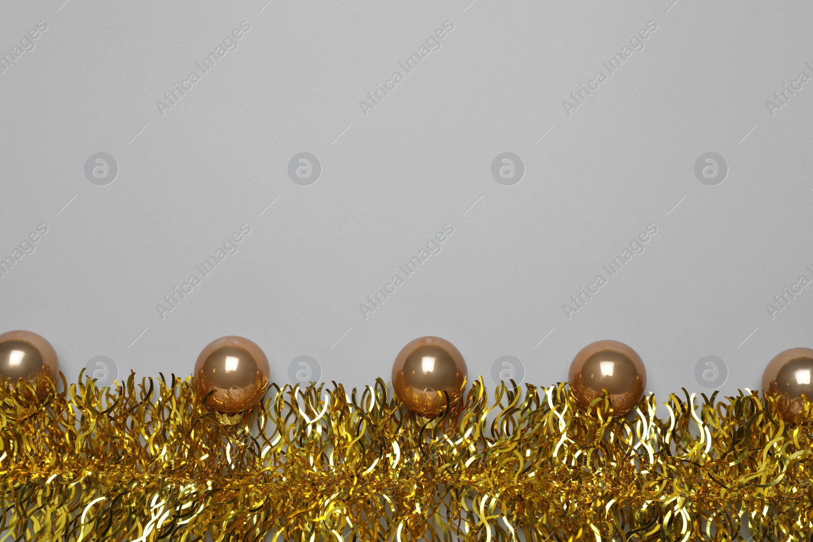 Photo of Golden tinsel and Christmas balls on light grey background, flat lay. Space for text