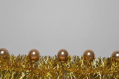 Golden tinsel and Christmas balls on light grey background, flat lay. Space for text
