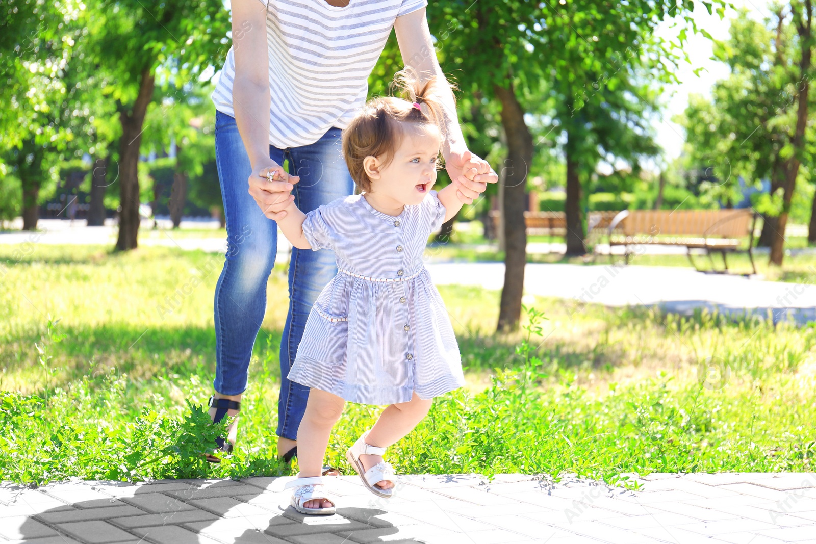 Photo of Adorable baby girl holding mother's hands while learning to walk outdoors