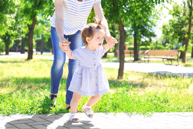 Adorable baby girl holding mother's hands while learning to walk outdoors