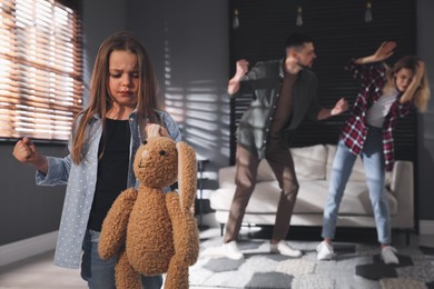 Photo of Little girl punishing toy bunny while her parents fighting on background, space for text. Domestic violence