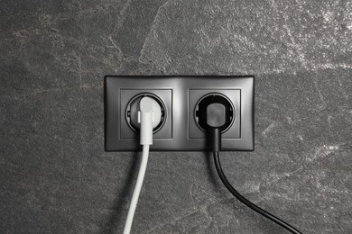 Power sockets with inserted plugs on dark grey wall. Electrical supply