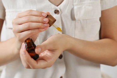 Photo of Young woman applying essential oil onto wrist on blurred background, closeup