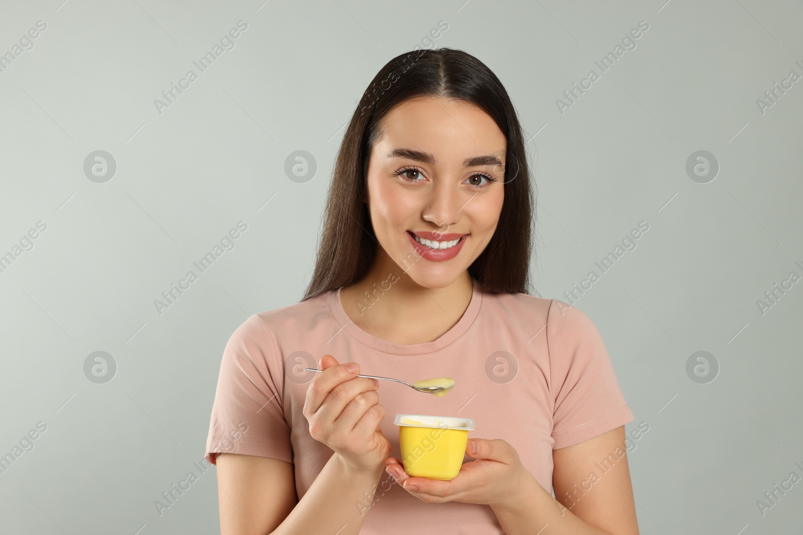 Photo of Portrait of happy woman with tasty yogurt on grey background