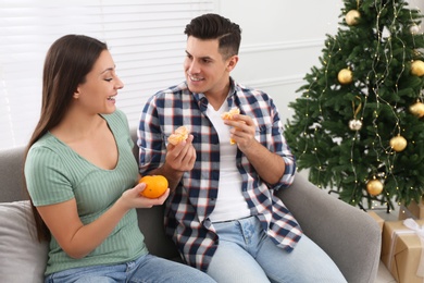 Photo of Happy couple with tangerines near Christmas tree indoors