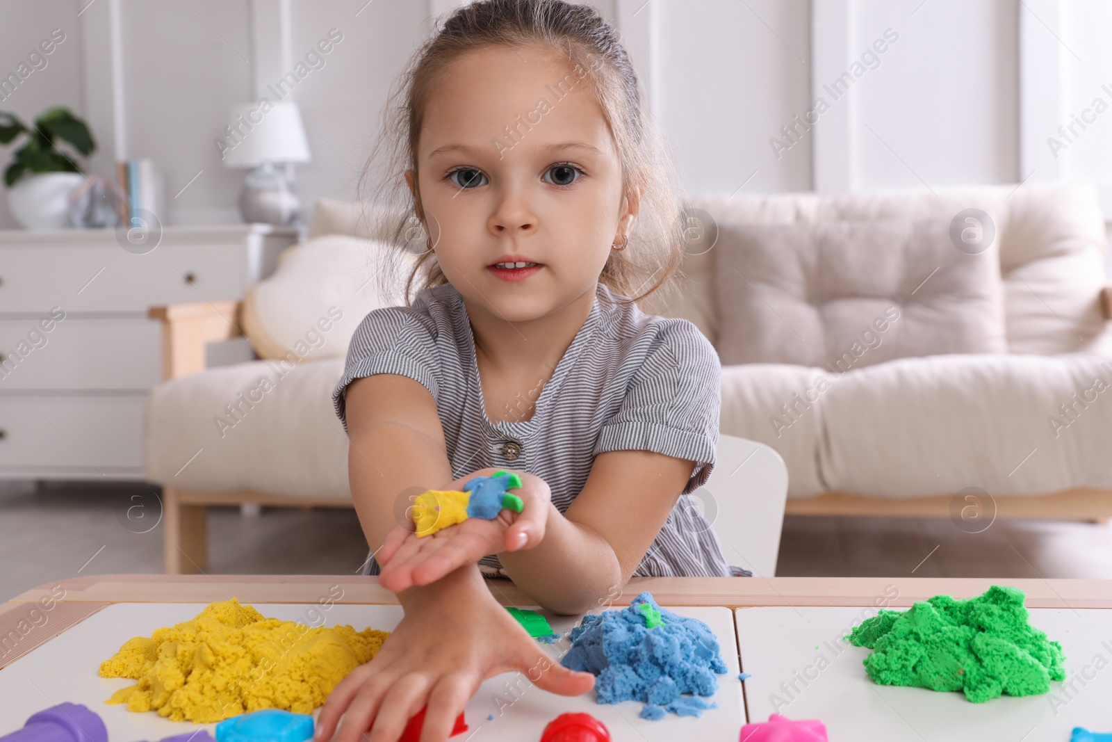 Photo of Cute little girl playing with bright kinetic sand at table in room