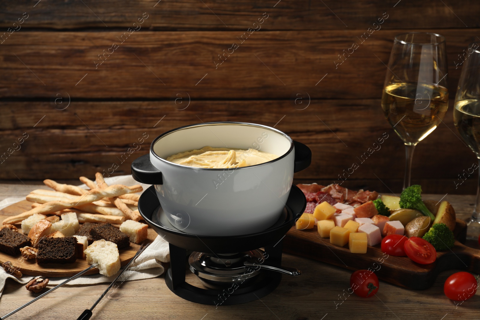 Photo of Tasty melted cheese in fondue pot, glasses of wine and snacks on wooden table