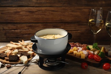 Tasty melted cheese in fondue pot, glasses of wine and snacks on wooden table