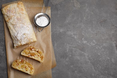 Photo of Delicious apple strudel with almonds and powdered sugar on grey table, flat lay. Space for text