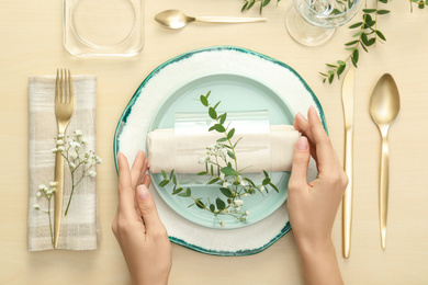 Woman setting table with green leaves for festive dinner, top view