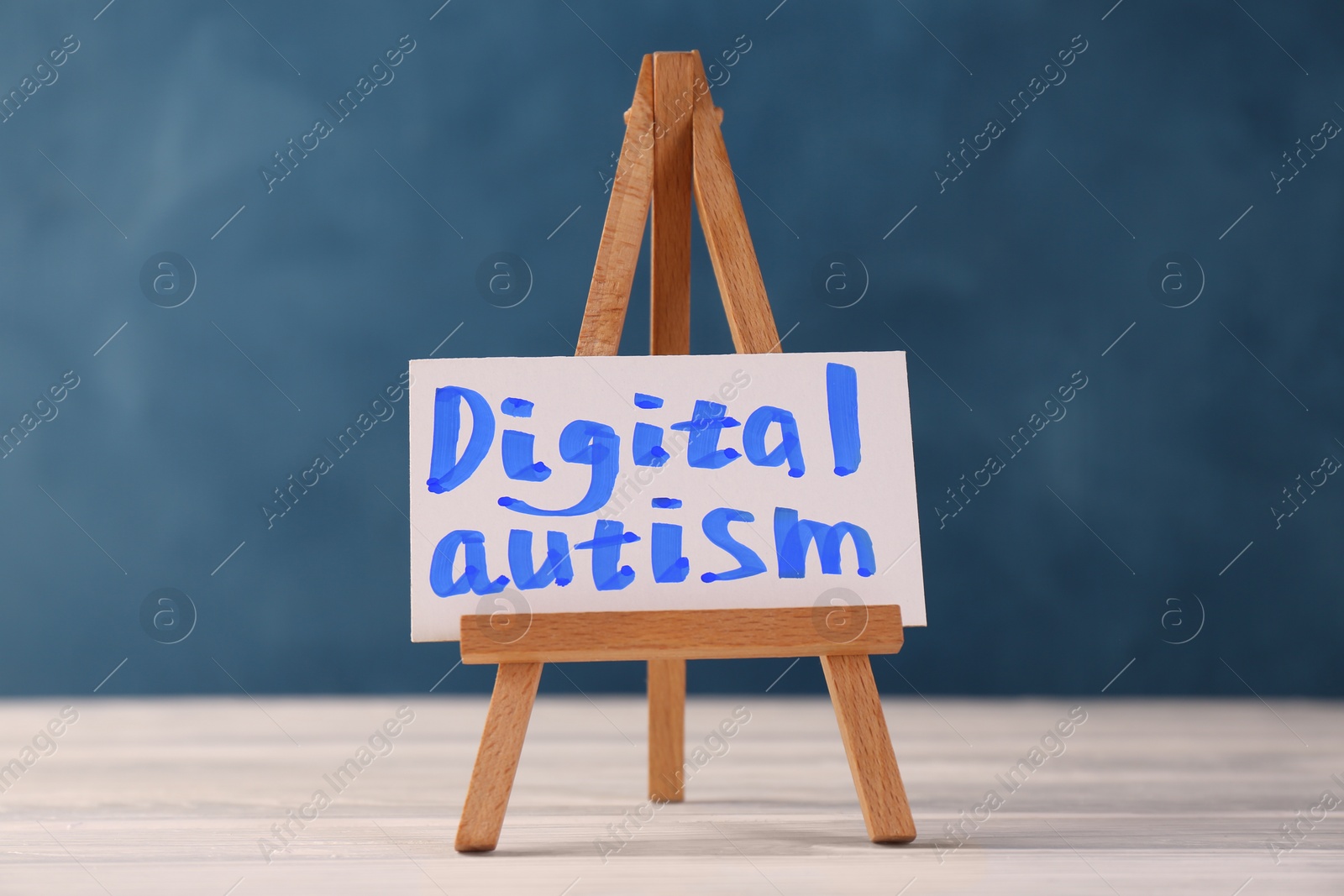 Photo of Mini easel with phrase Digital Autism on white wooden table