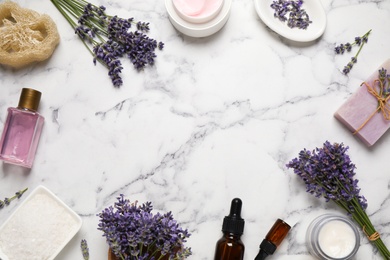 Frame of cosmetic products and lavender flowers on white marble table, flat lay. Space for text