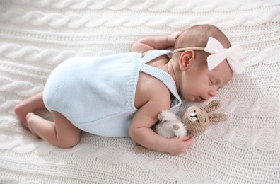 Photo of Adorable newborn baby with toy bunny sleeping on white knitted plaid, above view