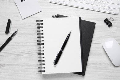Photo of Open blank notebook, keyboard and stationery on white wooden table, flat lay