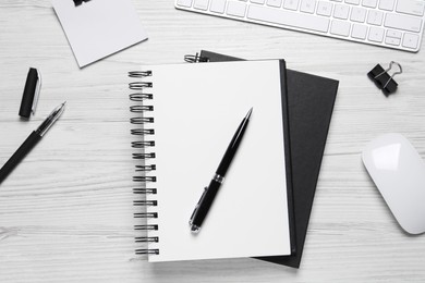 Open blank notebook, keyboard and stationery on white wooden table, flat lay