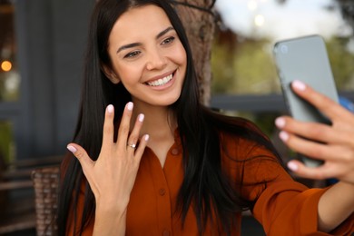 Happy woman with engagement ring taking selfie in outdoor cafe