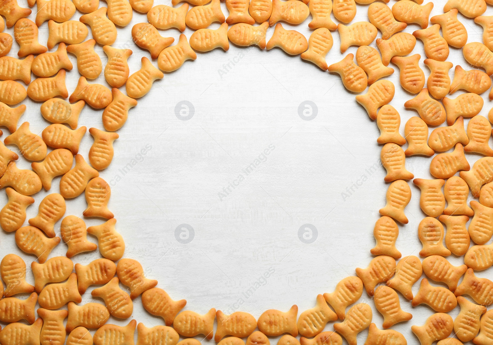 Photo of Frame of delicious goldfish crackers on white table. Space for text