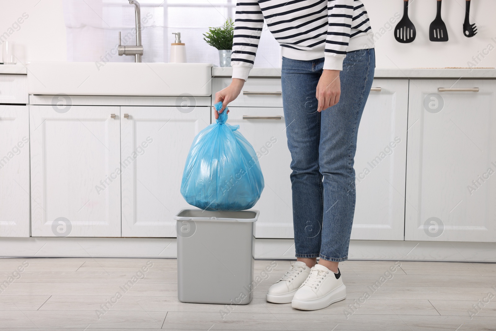 Photo of Woman taking garbage bag out of trash bin in kitchen, closeup