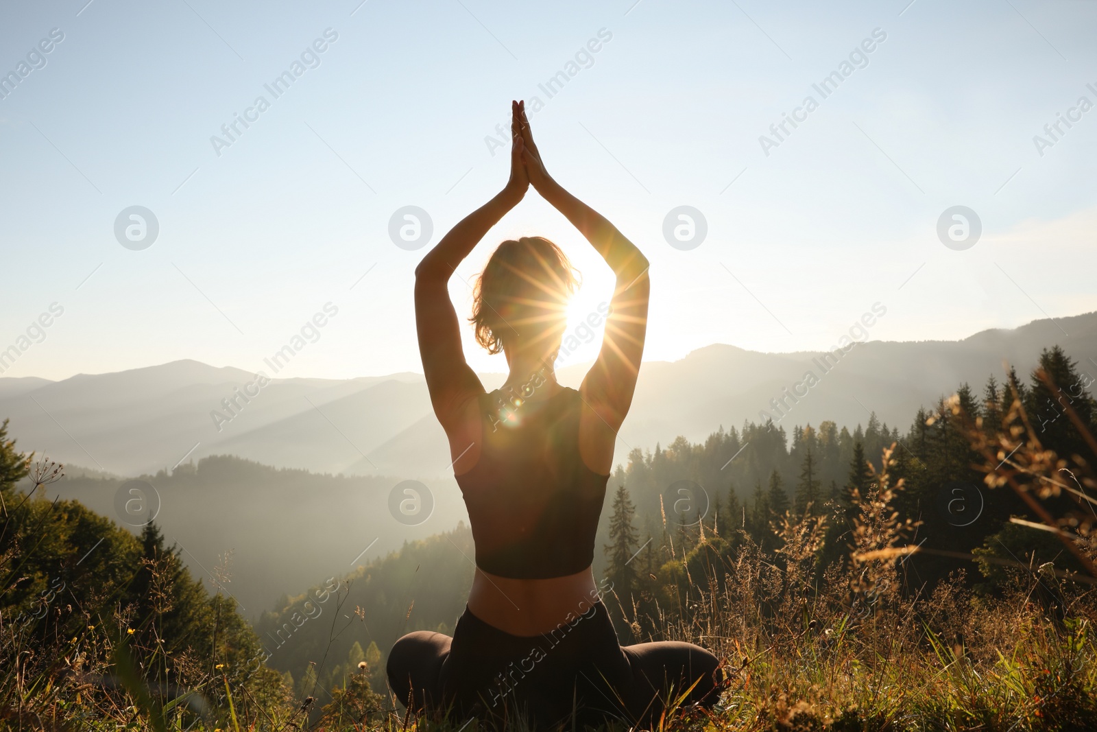 Image of Woman practicing yoga in mountains at sunrise, back view