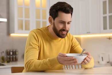 Man enjoying delicious soup at light table in kitchen