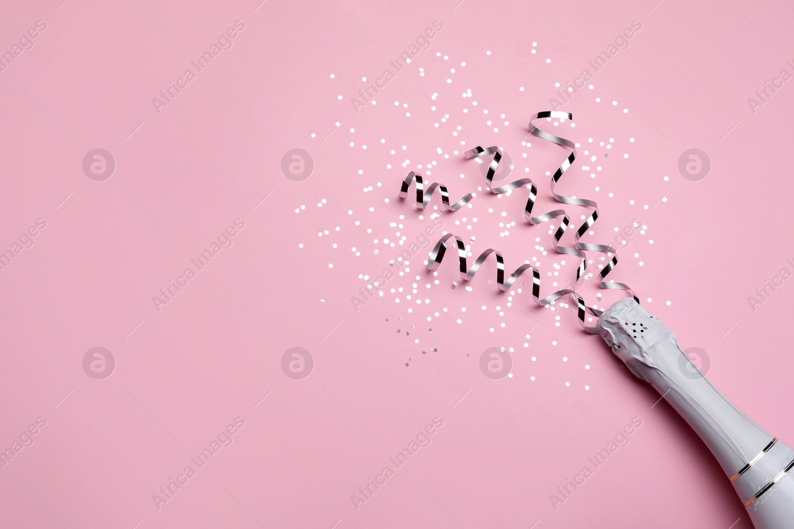 Photo of Bottle with champagne and shiny confetti on pink background, flat lay. Space for text