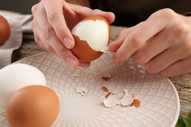 Photo of Woman peeling boiled egg at wooden table, closeup