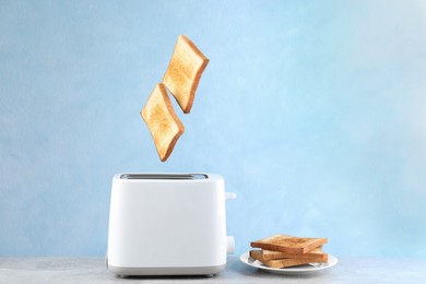 Bread slices popping up from modern toaster on white wooden table