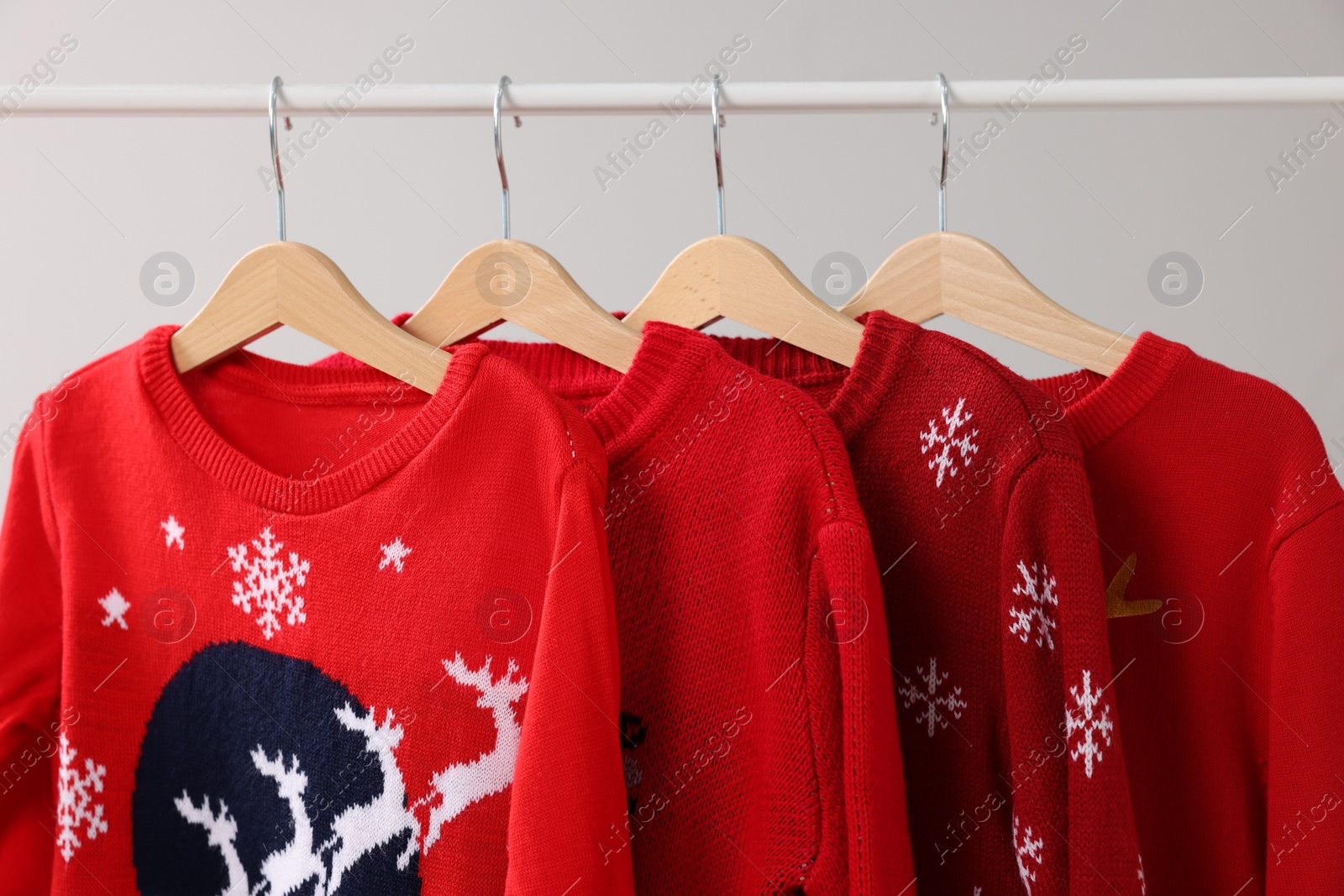 Photo of Different Christmas sweaters hanging on rack against light background, closeup