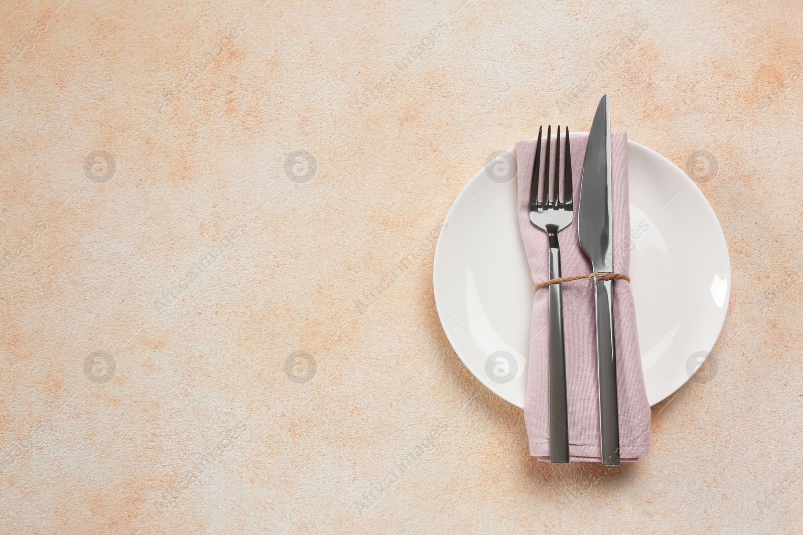 Photo of Plate, fork and knife on beige table, top view. Space for text