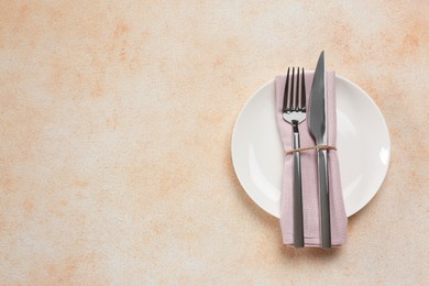 Photo of Plate, fork and knife on beige table, top view. Space for text