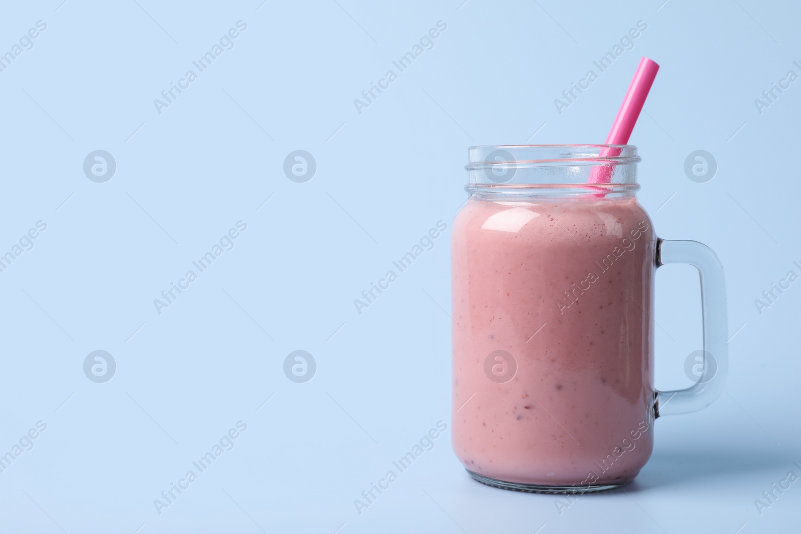 Photo of Mason jar with delicious berry smoothie on light blue background. Space for text