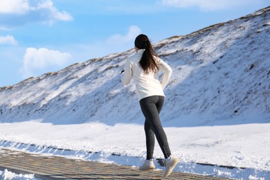 Photo of Woman running past snowy hill in winter. Outdoors sports exercises