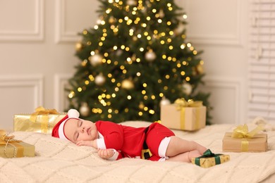 Photo of Cute baby in Christmas costume sleeping on knitted blanket against blurred festive lights. Winter holiday