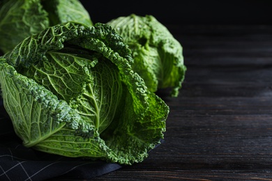 Photo of Fresh ripe savoy cabbages on black wooden table, closeup. Space for text
