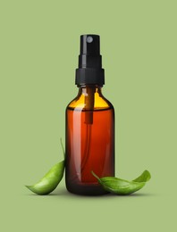 Image of Bottle of basil essential oil and green leaves on pale light green background