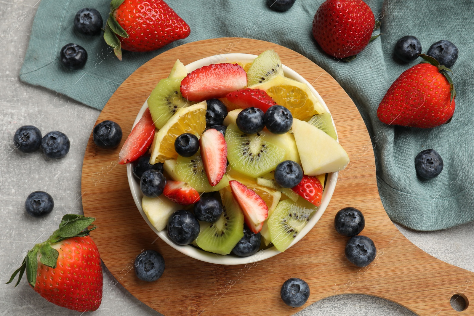 Photo of Tasty fruit salad in bowl and ingredients on gray textured table, flat lay