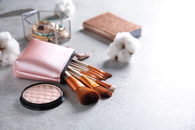 Photo of Cosmetic bag with professional makeup brushes and powder on light background