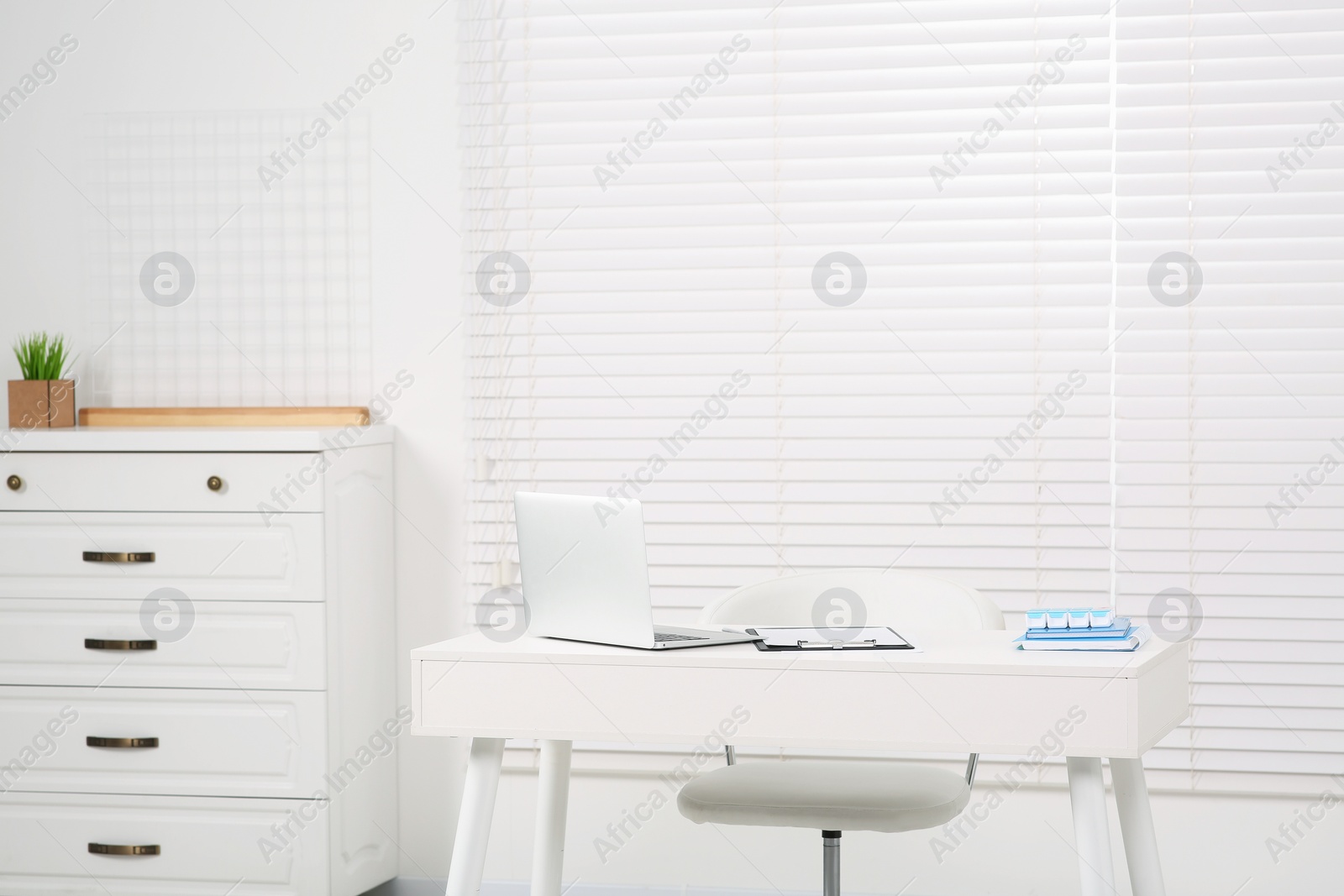 Photo of Beautiful office with laptop on white table, chair and chest of drawers. Doctor's workplace