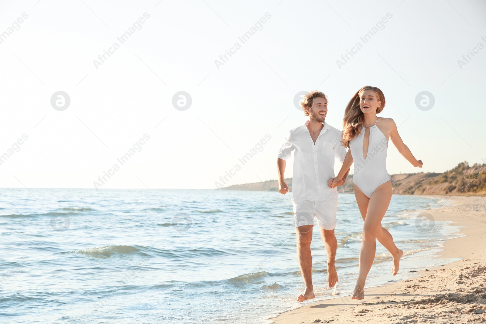 Photo of Happy young couple in beachwear running together on seashore. Space for text